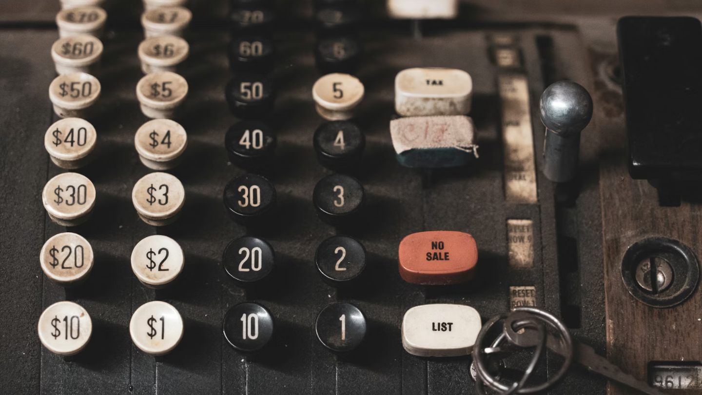 Ancienne caisse enregistreuse vintage avec boutons de prix en dollars, symbolisant le rapport qualité prix et la notion de coût dans un contexte commercial.